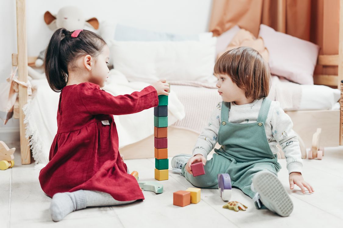 Duas crianças sentadas no chão brincando juntas com blocos de montar coloridos de encaixe